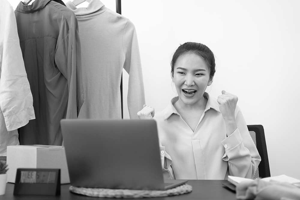 Small business owner Asian woman excited reading laptop screen.