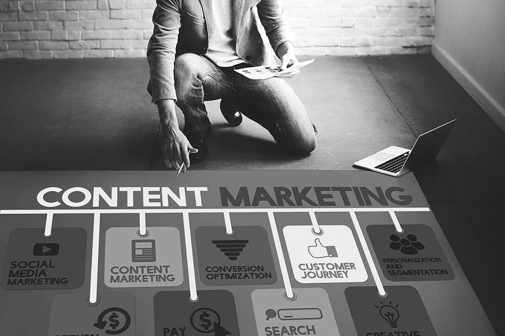 Casual businessman holding a document kneels on the floor over a Content Marketing diagram